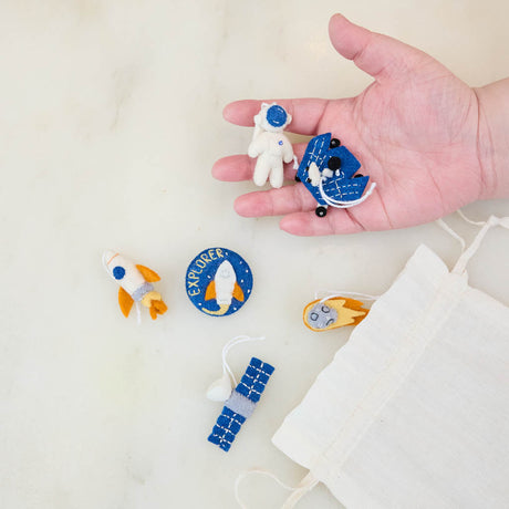 Blast off into a universe of discovery with our Space Mini Ornaments Set. This delightful collection includes five handcrafted felt ornaments inspired by the wonders of space: an astronaut, satellite, space shuttle, rocket ship, and meteor, along with a coordinating Explorer badge that can be displayed as a keepsake or worn as a symbol of curiosity and adventure.