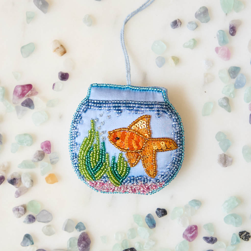 Make a splash with our whimsical Fishbowl Beaded Ornament! 🐠✨ This beautifully handcrafted ornament captures the charm of a beloved goldfish swimming peacefully through its miniature underwater world. Featuring a shimmering sequined goldfish, vibrant hand-beaded aquatic plants, and a sparkling fishbowl outlined with delicate glass beads, every detail is carefully stitched by hand to create a dazzling keepsake.