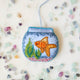 Make a splash with our whimsical Fishbowl Beaded Ornament! 🐠✨ This beautifully handcrafted ornament captures the charm of a beloved goldfish swimming peacefully through its miniature underwater world. Featuring a shimmering sequined goldfish, vibrant hand-beaded aquatic plants, and a sparkling fishbowl outlined with delicate glass beads, every detail is carefully stitched by hand to create a dazzling keepsake.