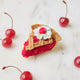 A true slice of nostalgia, our Cherry Pie Slice Ornament captures the timeless charm of one of America's favorite desserts. Handcrafted from natural wool felt, this delightful ornament features a rich cherry filling accented with sparkling red beadwork, a beautifully detailed lattice crust, a dollop of whipped cream, and a bright cherry on top.