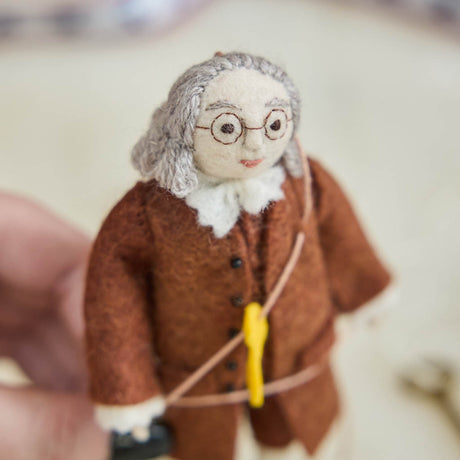 Honor the brilliance and ingenuity of a true American icon with our handcrafted Benjamin Franklin Ornament from the Craftspring Semiquincentennial Collection. Featuring Franklin in his classic colonial attire while flying a kite with a key