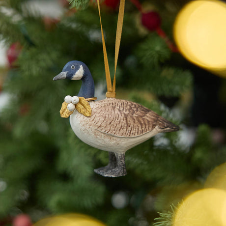 A vintage-inspired Canada Goose Resin Ornament, hand-painted in the Philippines with classic black-and-white markings, a golden metal holly necklace, and satin hanging ribbon.