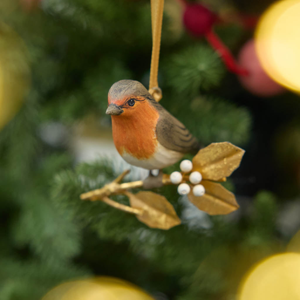 A vintage-inspired Robin Ornament, featuring a hand-painted red-breasted bird perched on a golden metal holly branch with white berries.