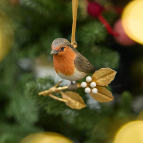 A vintage-inspired Robin Ornament, featuring a hand-painted red-breasted bird perched on a golden metal holly branch with white berries.