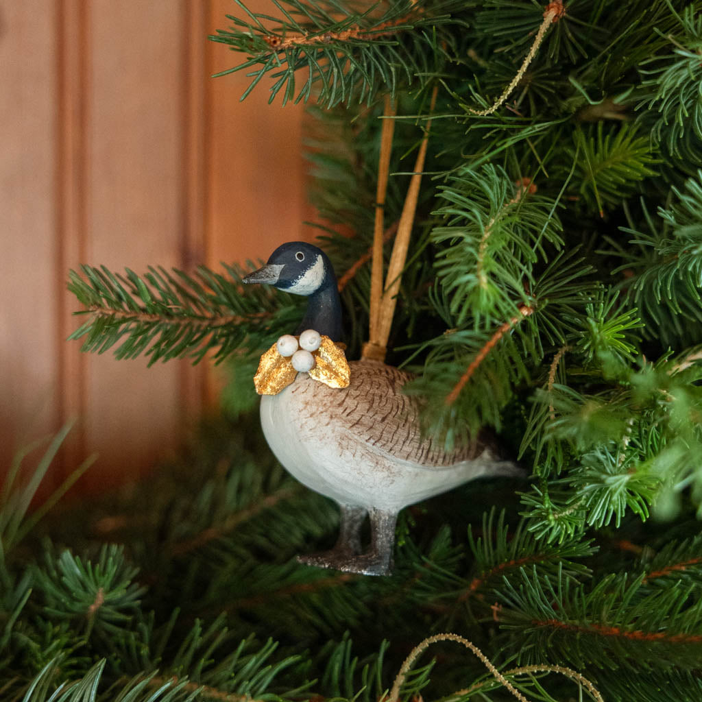 A vintage-inspired Canada Goose Resin Ornament, hand-painted in the Philippines with classic black-and-white markings, a golden metal holly necklace, and satin hanging ribbon.