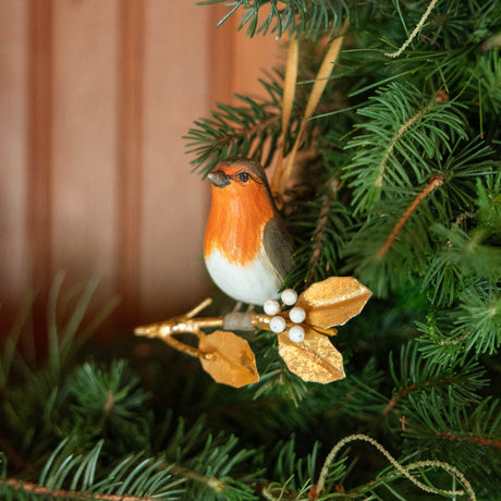 A vintage-inspired Robin Ornament, featuring a hand-painted red-breasted bird perched on a golden metal holly branch with white berries.