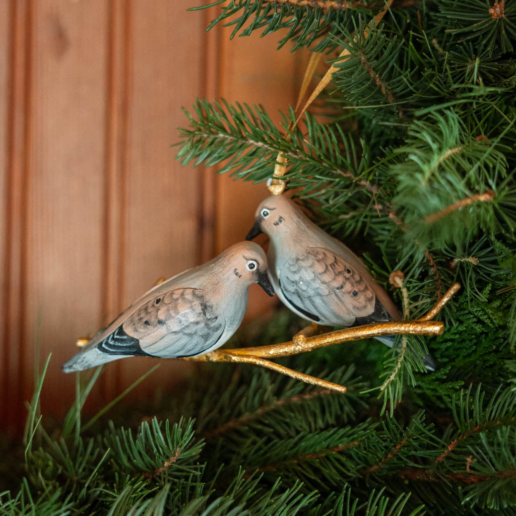 Two little doves, perched side by side. Our Mourning Doves Ornament captures one of nature’s sweetest pairings, with two beautifully hand-painted birds resting together on a delicate gold-toned metal branch.