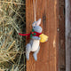 Our Gray Holiday Bunny with Chick Ornament captures a heartwarming moment of gentle friendship. Wrapped in a cozy red scarf adorned with festive holly leaves and tiny red berries, this sweet gray bunny lovingly cradles a fluffy yellow chick, creating a scene that's full of warmth, comfort, and Christmas cheer.