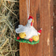 Gathered together on a festive green wreath our Holiday Hen with Chicks Ornament is a sweet celebration of family, nurturing, and holiday togetherness. A proud mother hen watches over her fluffy yellow chicks, while one festive little chick sports a tiny red Santa hat, adding an extra dash of Christmas cheer. 