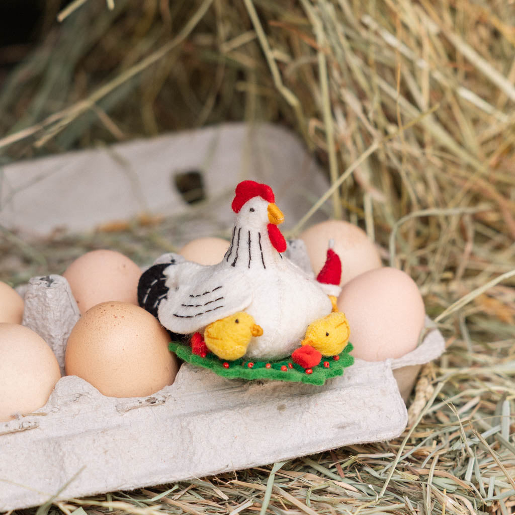 Gathered together on a festive green wreath our Holiday Hen with Chicks Ornament is a sweet celebration of family, nurturing, and holiday togetherness. A proud mother hen watches over her fluffy yellow chicks, while one festive little chick sports a tiny red Santa hat, adding an extra dash of Christmas cheer. 