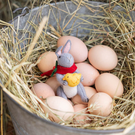 Our Gray Holiday Bunny with Chick Ornament captures a heartwarming moment of gentle friendship. Wrapped in a cozy red scarf adorned with festive holly leaves and tiny red berries, this sweet gray bunny lovingly cradles a fluffy yellow chick, creating a scene that's full of warmth, comfort, and Christmas cheer.