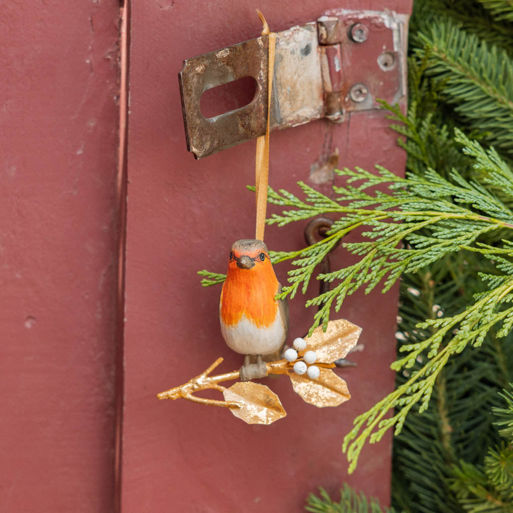 A vintage-inspired Robin Ornament, featuring a hand-painted red-breasted bird perched on a golden metal holly branch with white berries.