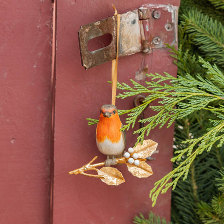 A vintage-inspired Robin Ornament, featuring a hand-painted red-breasted bird perched on a golden metal holly branch with white berries.