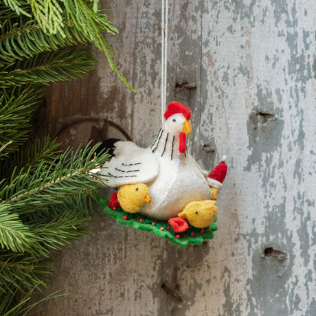 Gathered together on a festive green wreath our Holiday Hen with Chicks Ornament is a sweet celebration of family, nurturing, and holiday togetherness. A proud mother hen watches over her fluffy yellow chicks, while one festive little chick sports a tiny red Santa hat, adding an extra dash of Christmas cheer. 