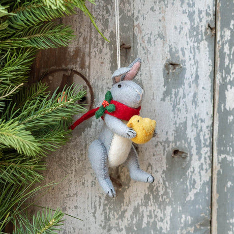 Our Gray Holiday Bunny with Chick Ornament captures a heartwarming moment of gentle friendship. Wrapped in a cozy red scarf adorned with festive holly leaves and tiny red berries, this sweet gray bunny lovingly cradles a fluffy yellow chick, creating a scene that's full of warmth, comfort, and Christmas cheer.