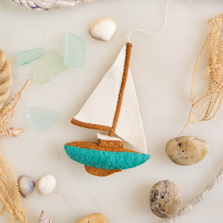 Set sail for holiday memories with our handcrafted Sailboat Ornament, a charming tribute to life on the water. Featuring crisp white sails, a warm wood-toned mast and deck, and a sea-glass-inspired turquoise hull, this classic sailboat captures the quiet beauty of coastal living and the freedom of open water.