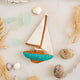 Set sail for holiday memories with our handcrafted Sailboat Ornament, a charming tribute to life on the water. Featuring crisp white sails, a warm wood-toned mast and deck, and a sea-glass-inspired turquoise hull, this classic sailboat captures the quiet beauty of coastal living and the freedom of open water.