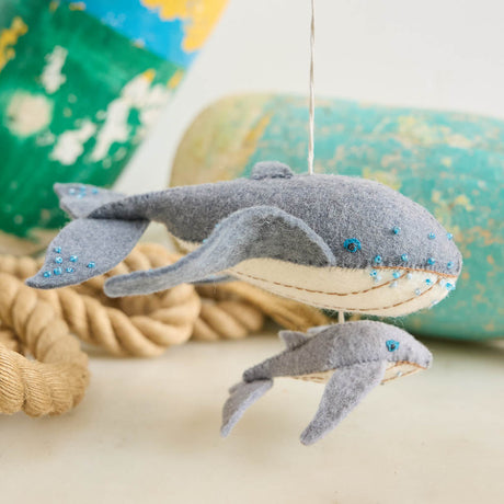 Graceful, gentle, and full of wonder, our Humpback Whale with Baby Ornament captures one of nature’s most touching sights—a mother whale guiding her calf through the open sea. Handcrafted from soft felted wool and accented with shimmering blue beadwork, this beautiful ornament celebrates the deep connection between parent and child while honoring the majestic marine life that frequents Maine’s coastal waters.