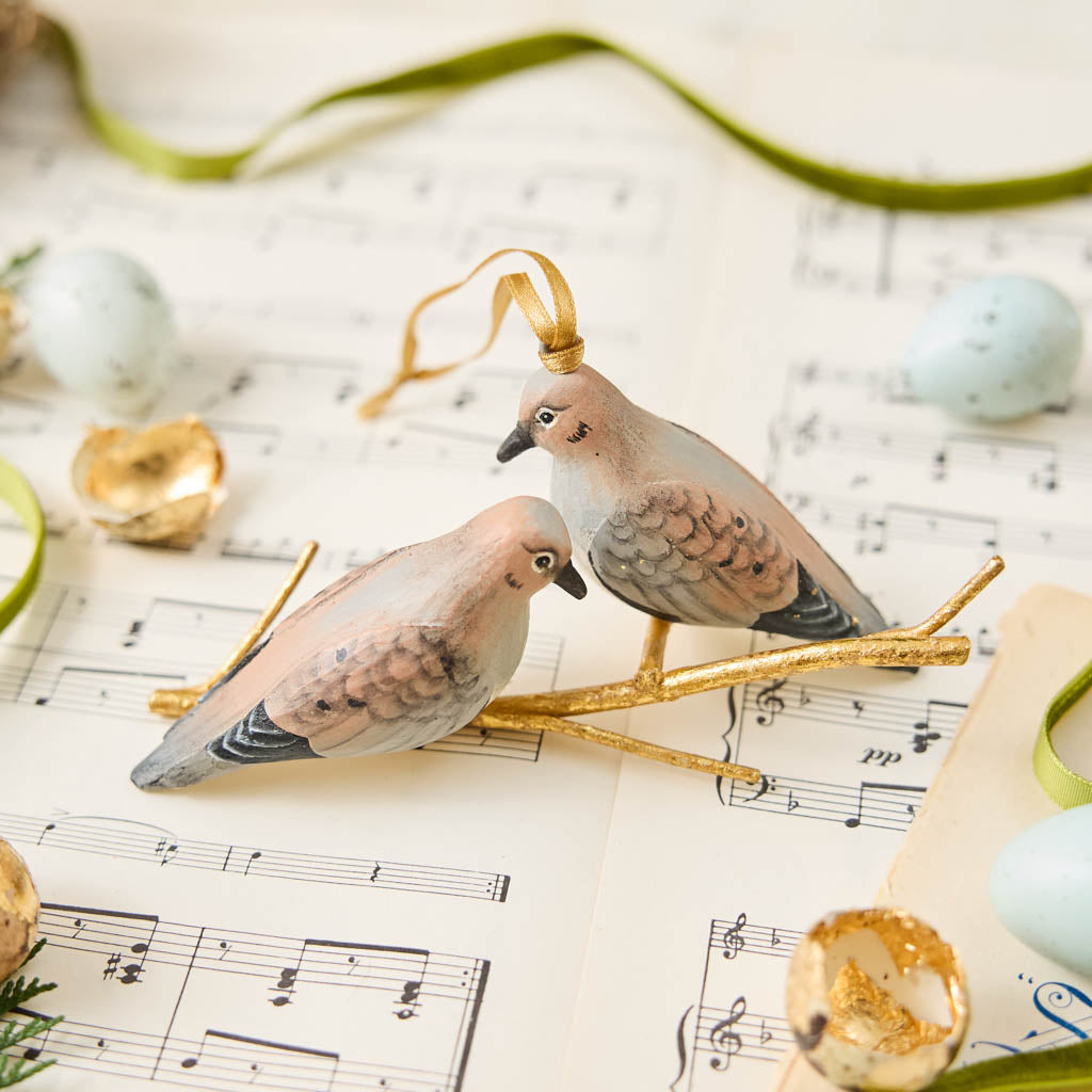 Two little doves, perched side by side. Our Mourning Doves Ornament captures one of nature’s sweetest pairings, with two beautifully hand-painted birds resting together on a delicate gold-toned metal branch.
