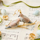 Two little doves, perched side by side. Our Mourning Doves Ornament captures one of nature’s sweetest pairings, with two beautifully hand-painted birds resting together on a delicate gold-toned metal branch.