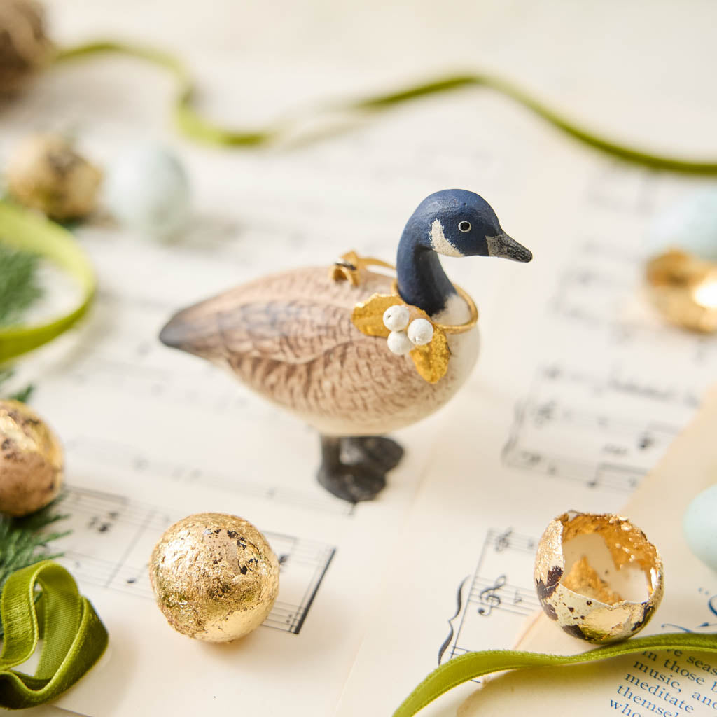 A vintage-inspired Canada Goose Resin Ornament, hand-painted in the Philippines with classic black-and-white markings, a golden metal holly necklace, and satin hanging ribbon.