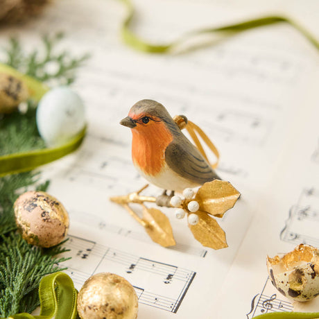A vintage-inspired Robin Ornament, featuring a hand-painted red-breasted bird perched on a golden metal holly branch with white berries.