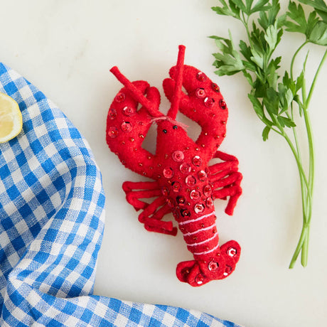 Commemorate the bounty of the northeastern seaboard with our handcrafted Bejeweled Red Lobster Ornament, designed to bring the spirit of coastal Maine to your home. Crafted from vibrant red felt and embellished with sparkling beads and sequins, this festive lobster ornament catches the light beautifully, adding texture, shimmer, and whimsical seaside charm to your holiday décor.