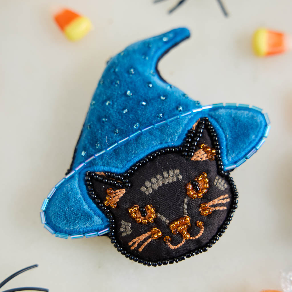 A double-sided handmade Black Cat Beaded Ornament featuring an intricately embroidered cat in a sparkling blue witch hat, with a playful “Boo” on the reverse.