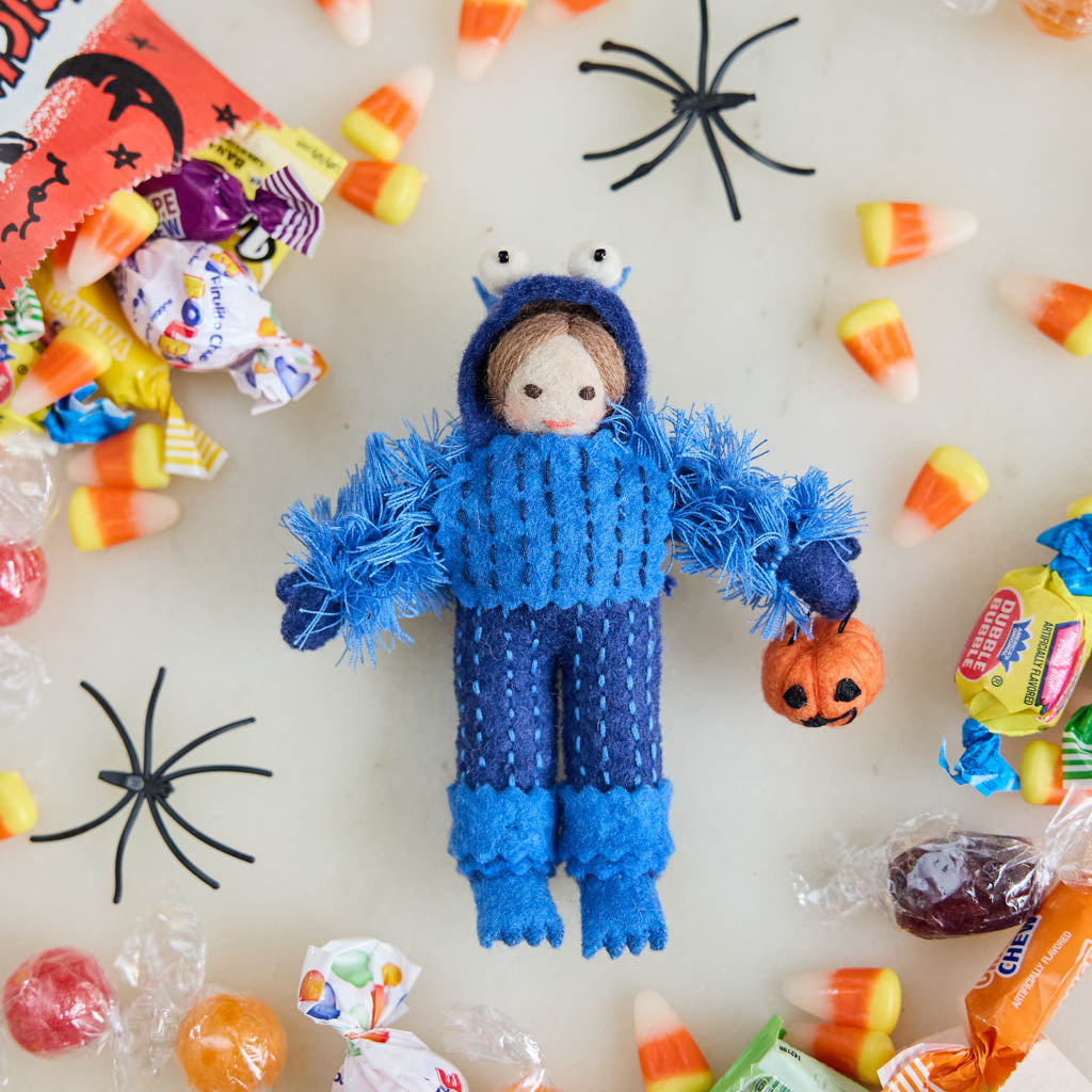 A handmade felt Monster Trick-or-Treater Ornament featuring a child dressed in a fuzzy blue monster costume and carrying a miniature jack-o’-lantern candy bucket.