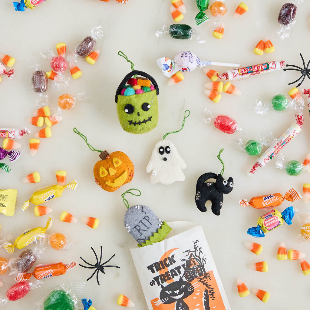 A handmade felt Halloween Mini Ornaments Set featuring five tiny spooky-season favorites: a black cat, candy-filled monster bucket, ghost, jack-o’-lantern, and RIP tombstone.