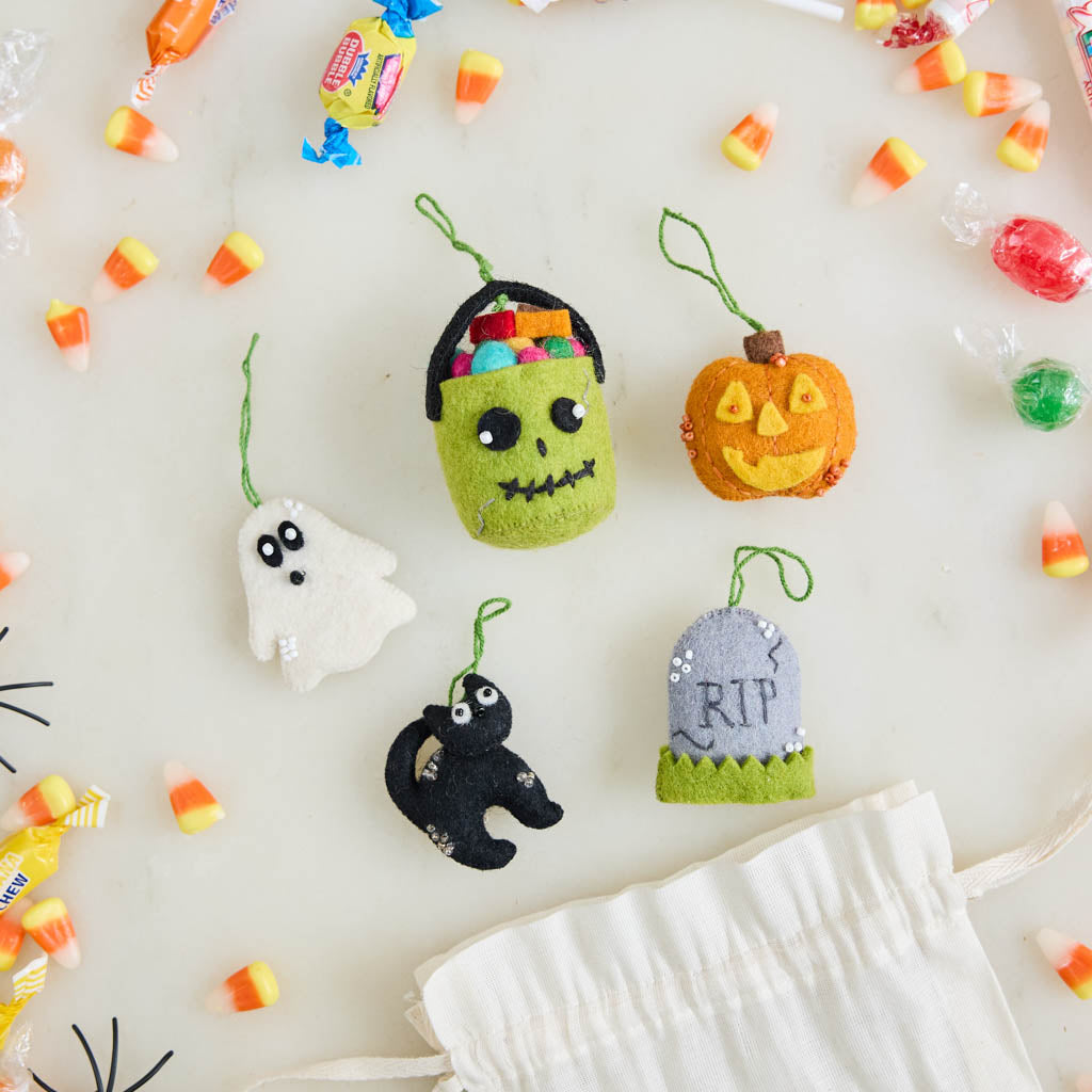 A handmade felt Halloween Mini Ornaments Set featuring five tiny spooky-season favorites: a black cat, candy-filled monster bucket, ghost, jack-o’-lantern, and RIP tombstone.