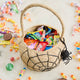 A hand-crocheted raffia Spider Basket featuring a bold black spiderweb and playful spider detail, perfectly sized for trick-or-treating, Halloween treasures, and festive fall displays.