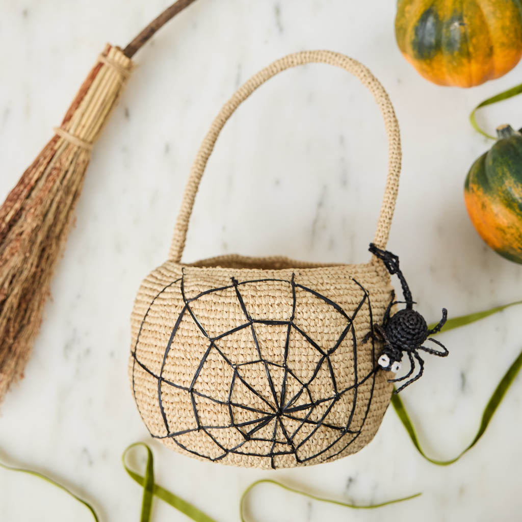 A hand-crocheted raffia Spider Basket featuring a bold black spiderweb and playful spider detail, perfectly sized for trick-or-treating, Halloween treasures, and festive fall displays.