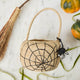 A hand-crocheted raffia Spider Basket featuring a bold black spiderweb and playful spider detail, perfectly sized for trick-or-treating, Halloween treasures, and festive fall displays.