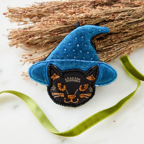 A double-sided handmade Black Cat Beaded Ornament featuring an intricately embroidered cat in a sparkling blue witch hat, with a playful “Boo” on the reverse.