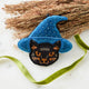 A double-sided handmade Black Cat Beaded Ornament featuring an intricately embroidered cat in a sparkling blue witch hat, with a playful “Boo” on the reverse.