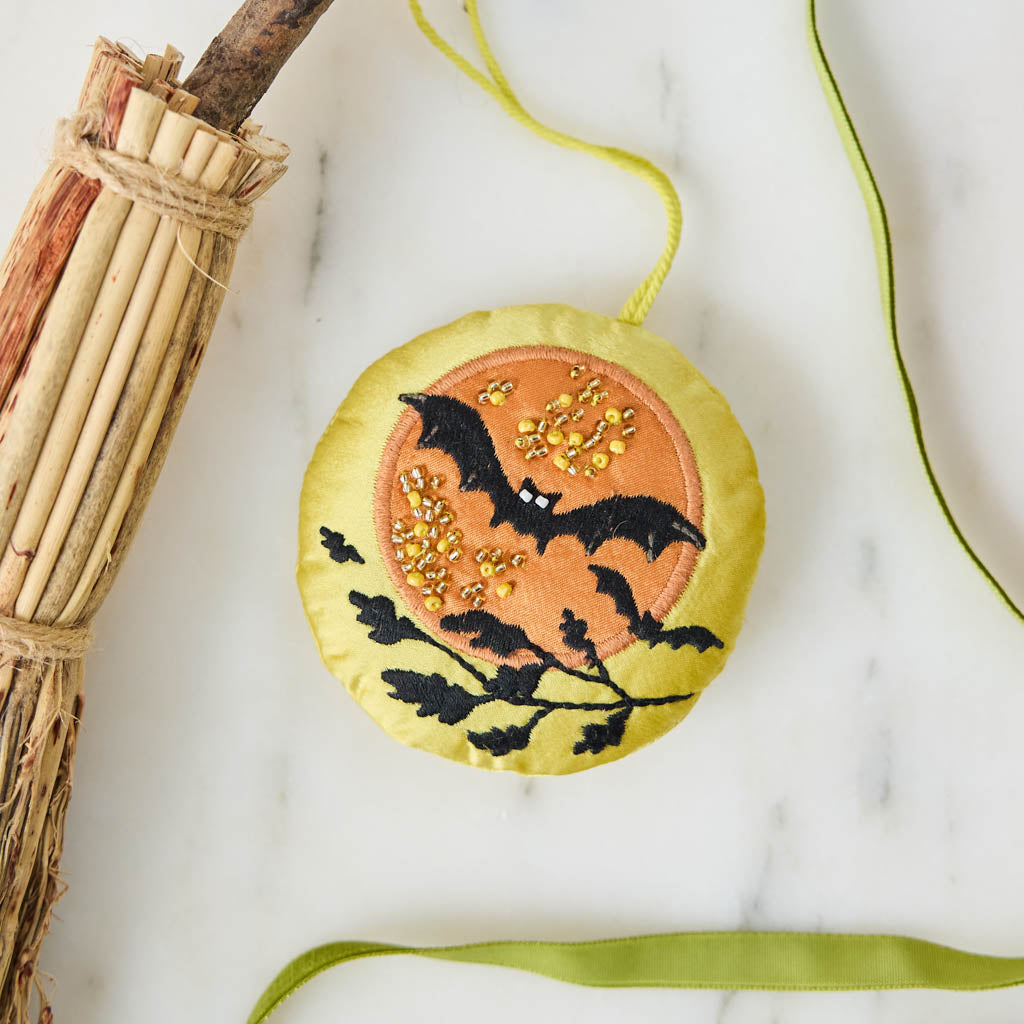 A double-sided handmade beaded Bat &amp; Moon Ornament featuring embroidered bats flying across a glowing full moon, with a playful “Swoop” design on the reverse.