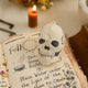A handmade felted and embroidered Human Skull Ornament featuring embroidered bone, teeth, and crack details for a delightfully spooky addition to Halloween décor.