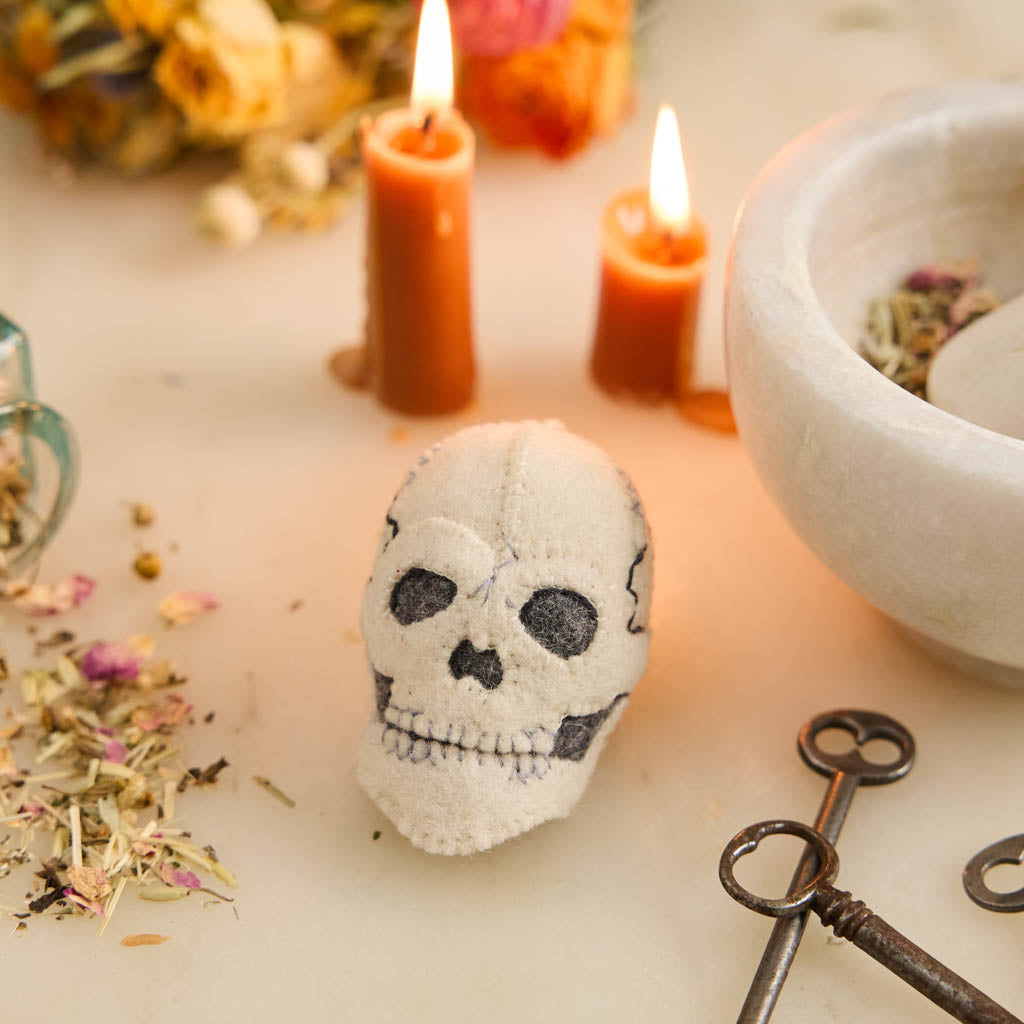 A handmade felted and embroidered Human Skull Ornament featuring embroidered bone, teeth, and crack details for a delightfully spooky addition to Halloween décor.