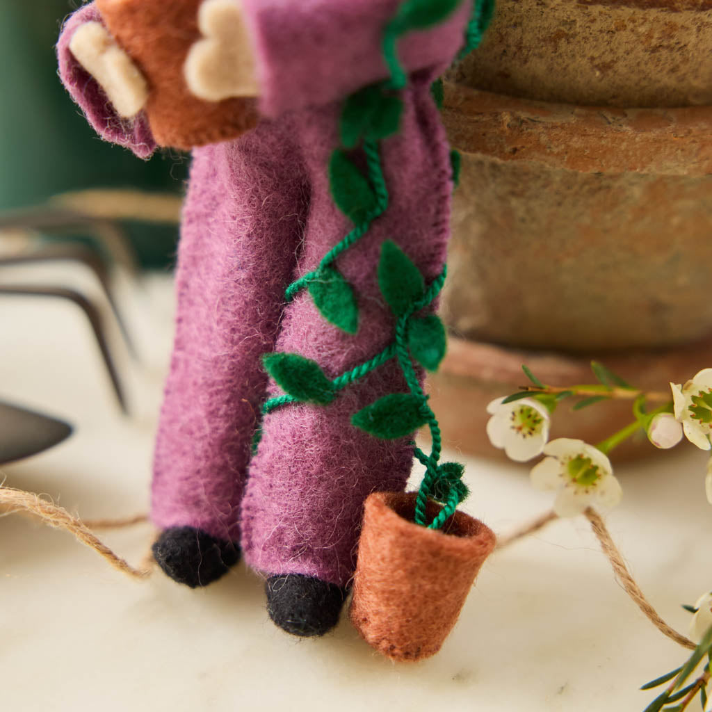 For the person who always has room for just one more plant, our Plant Parent Ornament celebrates the love, care, and wonderfully leafy obsession of keeping a home full of green things. Handcrafted from natural wool by skilled artisans, this whimsical felt ornament features a proud plant parent dressed in purple and happily surrounded by an abundance of potted greenery.