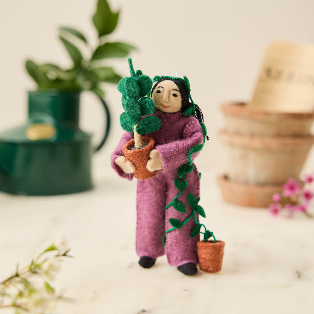 For the person who always has room for just one more plant, our Plant Parent Ornament celebrates the love, care, and wonderfully leafy obsession of keeping a home full of green things. Handcrafted from natural wool by skilled artisans, this whimsical felt ornament features a proud plant parent dressed in purple and happily surrounded by an abundance of potted greenery.