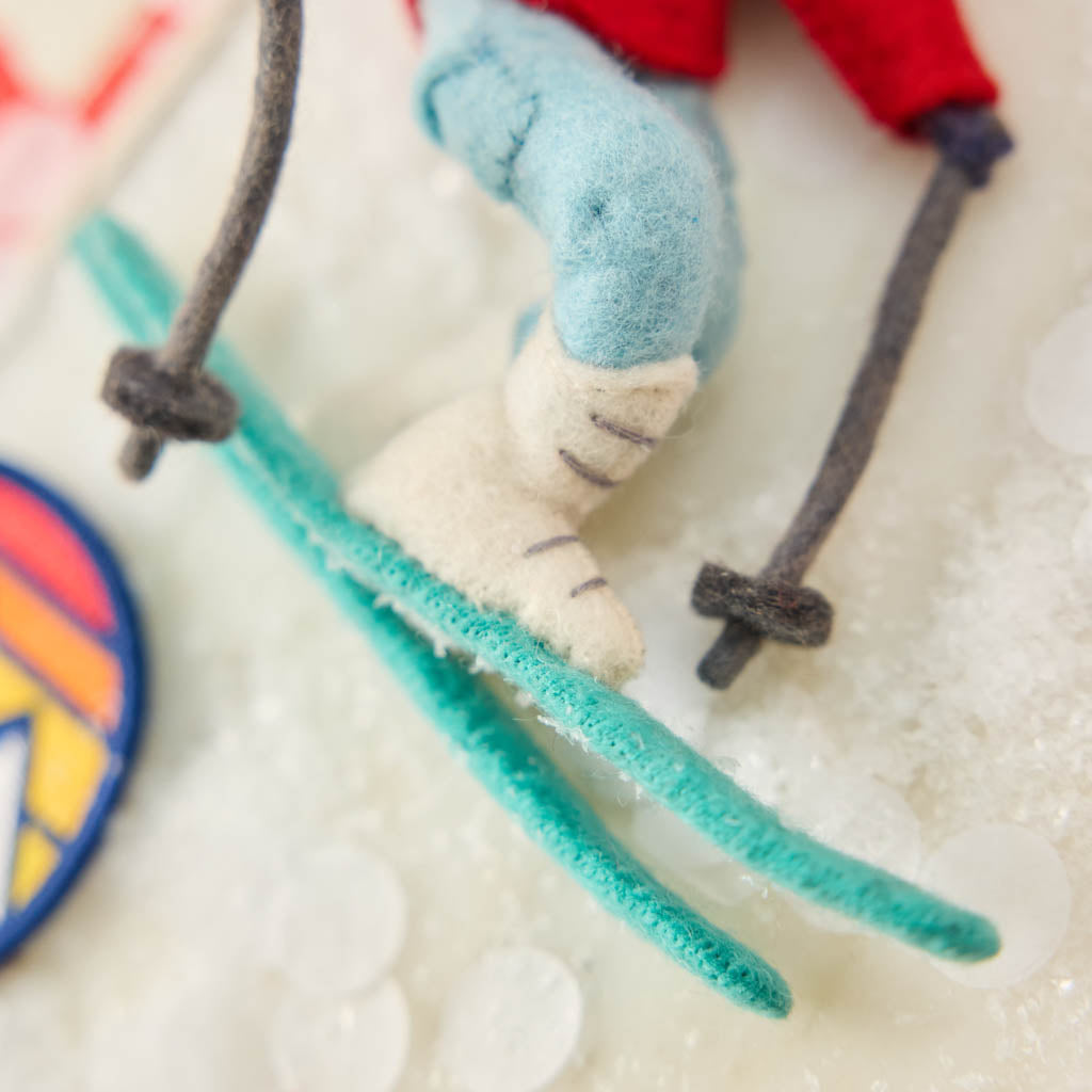 Our Alpine Skier Ornament is ready to carve through the holiday season in style. Dressed in a bright red ski jacket, powder-blue pants, and matching goggles, this spirited skier comes complete with turquoise skis and poles, capturing the thrill of a perfect day on the mountain.
