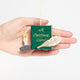 Miniature hand-felted wool ornament shaped like an open book titled A Christmas Carol, featuring embroidered details including a writing plume and a golden chamberstick. Crafted from merino-blend wool with a hanging string, the ornament evokes Victorian charm and the classic story of Ebenezer Scrooge. Measures approximately 2.25 inches high and 3.75 inches wide. Held in hand for scale.
