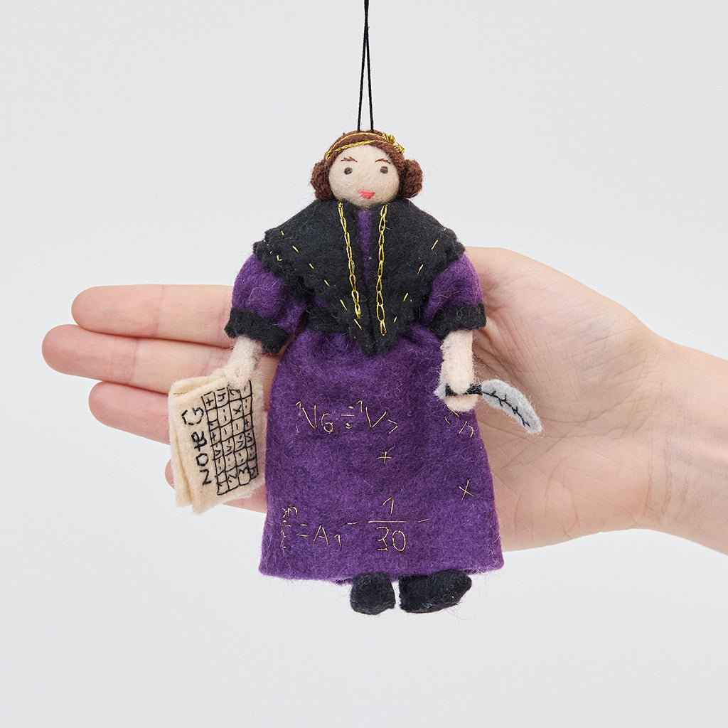 Craftspring’s Ada Lovelace ornament held in front of a hand to show its size—handmade from sustainable wool with intricate beaded and embroidered details including her holding Note G and gold embroidered equations on her dress, ethically crafted by artisans using sustainable wool.