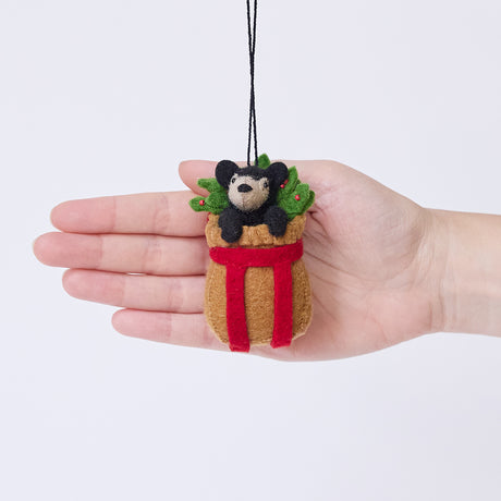 Craftspring’s Adirondack Basket with Black Bear Cub ornament held in front of a hand to show its size—handmade from sustainable wool with a rustic basket, holly, and a cute black bear cub, ethically crafted by artisans using sustainable wool.