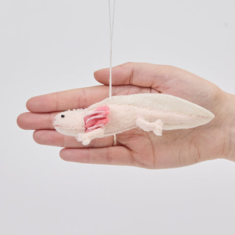 Craftspring’s Axolotl ornament held in front of a hand to show its size—handmade from sustainable wool with a cute pink design and intricate embroidered and beaded details, ethically crafted by artisans using sustainable wool.
