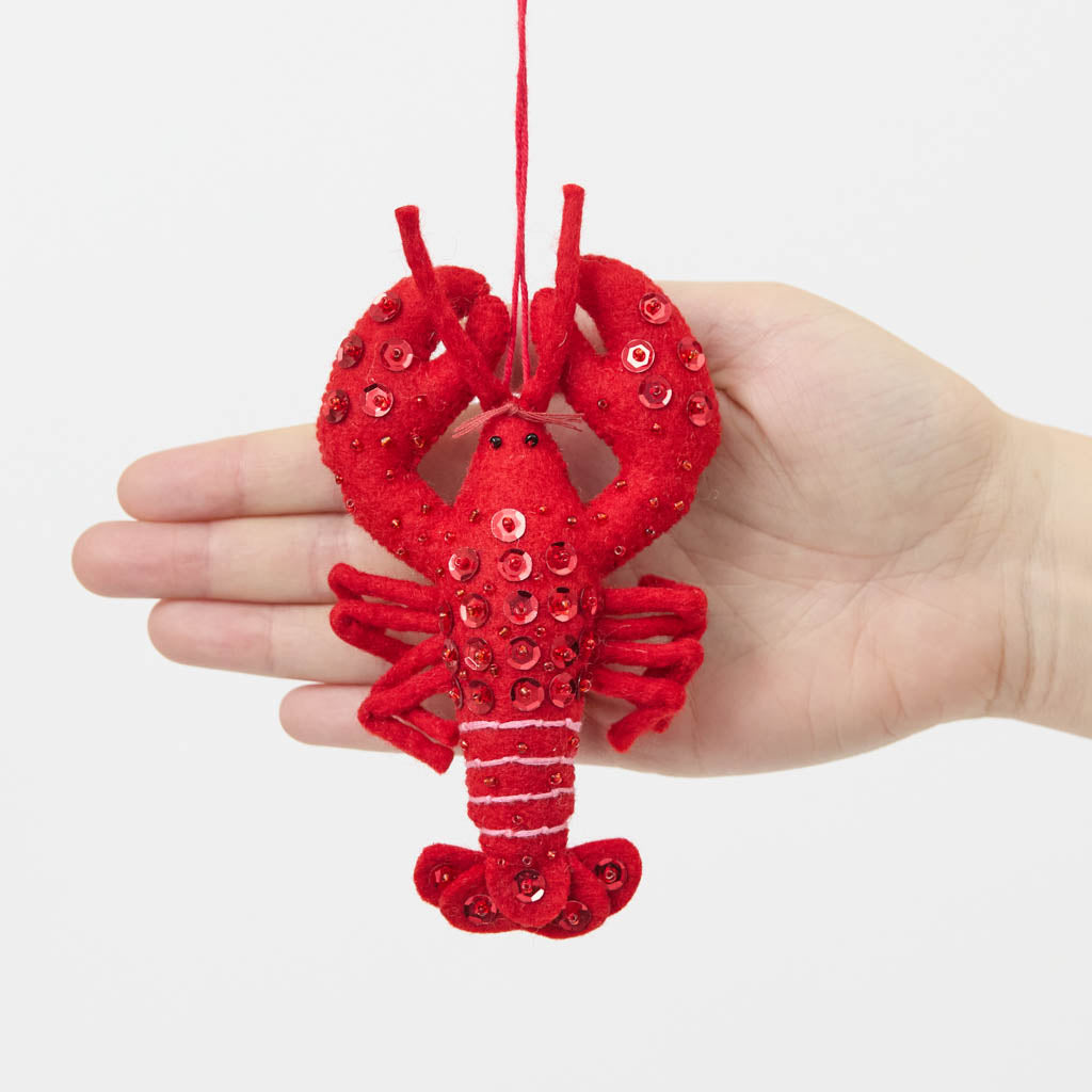 Commemorate the bounty of the northeastern seaboard with our handcrafted Bejeweled Red Lobster Ornament, designed to bring the spirit of coastal Maine to your home. Crafted from vibrant red felt and embellished with sparkling beads and sequins, this festive lobster ornament catches the light beautifully, adding texture, shimmer, and whimsical seaside charm to your holiday décor.