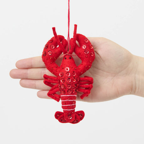 Commemorate the bounty of the northeastern seaboard with our handcrafted Bejeweled Red Lobster Ornament, designed to bring the spirit of coastal Maine to your home. Crafted from vibrant red felt and embellished with sparkling beads and sequins, this festive lobster ornament catches the light beautifully, adding texture, shimmer, and whimsical seaside charm to your holiday décor.
