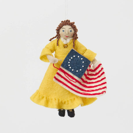 Celebrate the legendary maker associated with America’s first flag with our handcrafted Betsy Ross Ornament. Dressed in a bright colonial gown and holding the iconic early American flag, Betsy honors the spirit of independence, ingenuity, and handmade tradition.