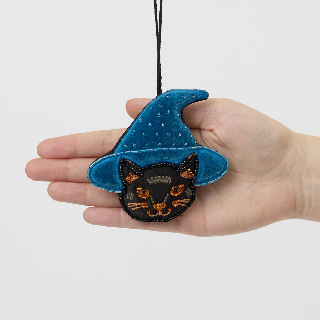 A double-sided handmade Black Cat Beaded Ornament featuring an intricately embroidered cat in a sparkling blue witch hat, with a playful “Boo” on the reverse.